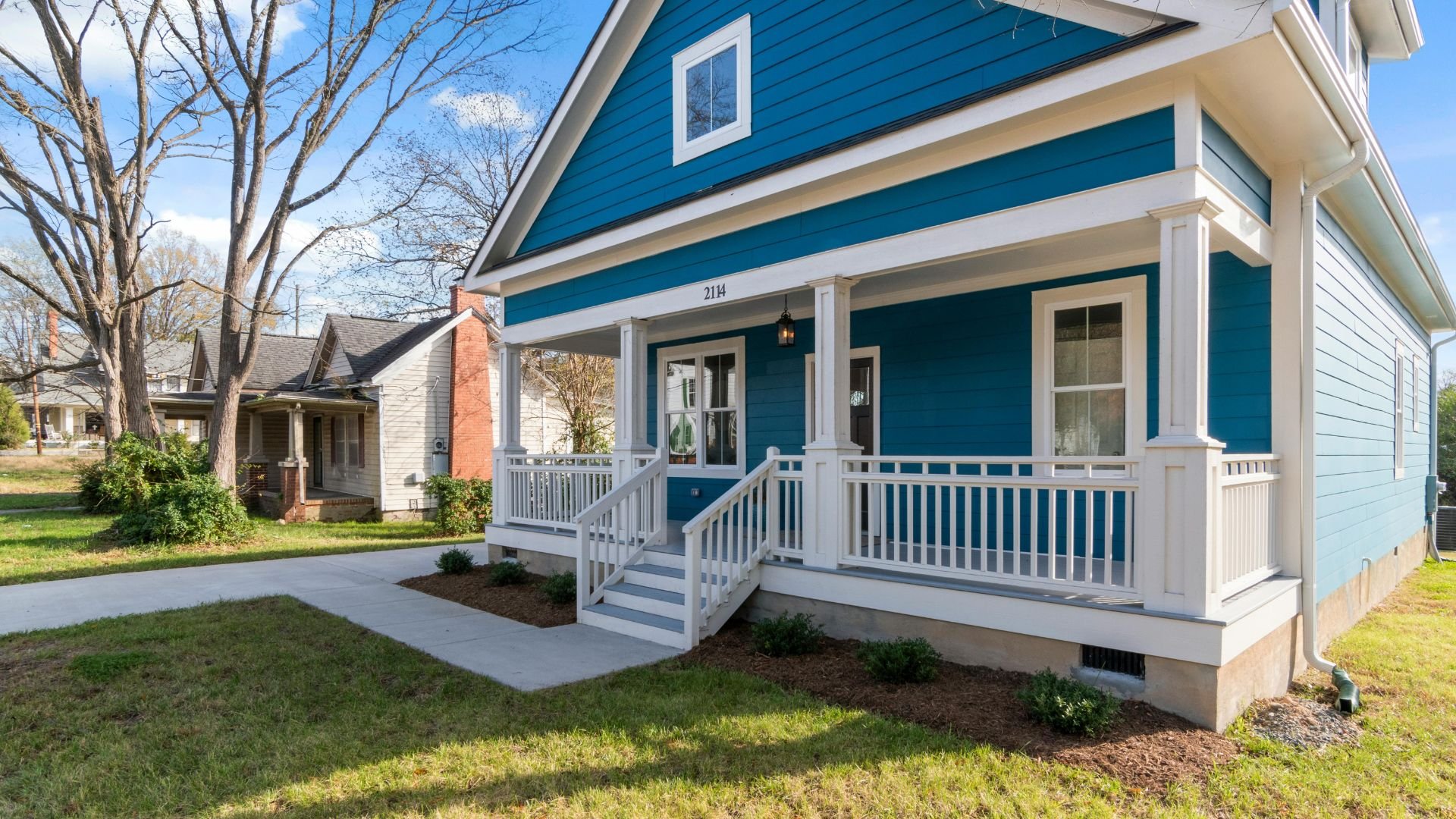Blue two-story house with white porch and railing on residential street
