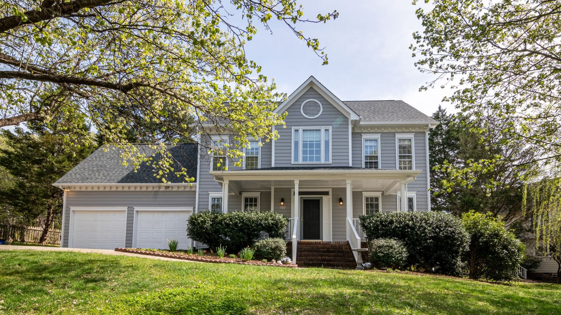 Two-story gray house with white trim and green trees in spring